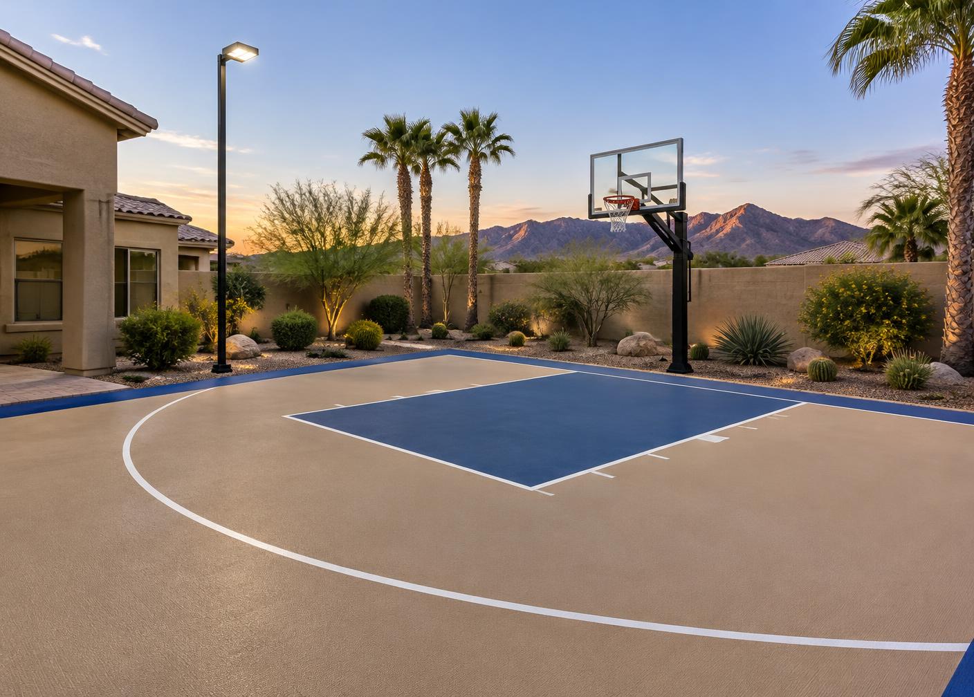 Tan and blue backyard basketball half court with an in-ground hoop and a court light